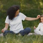 Mother and daughter bonding through yoga outdoors in a serene grassy field.